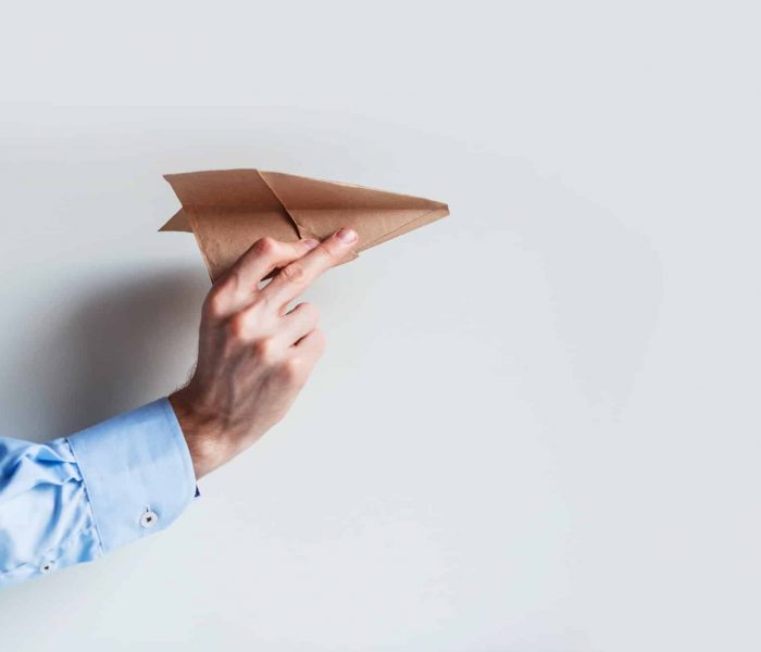 A male hand in a blue shirt uniform launches a paper airplane.